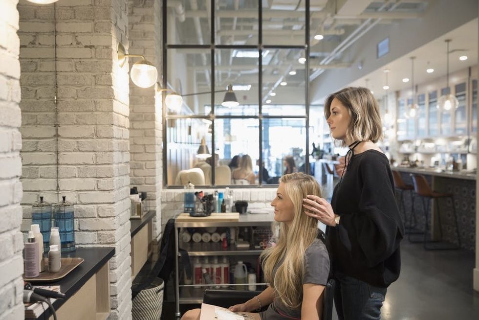 Woman styling another woman's hair at a salon. 