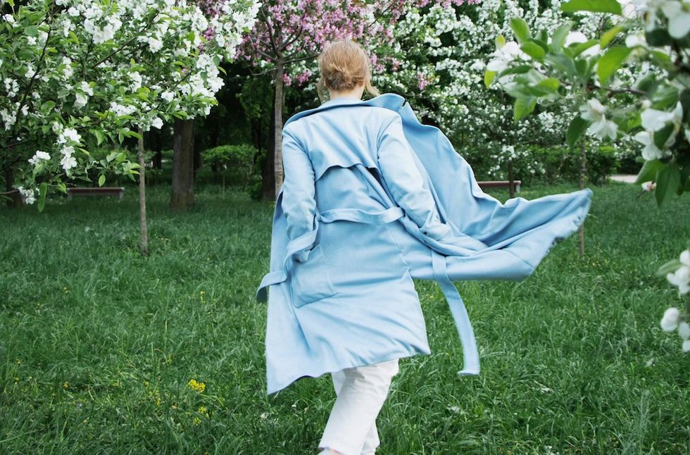 woman walking in the grass wearing a blue trench coat
