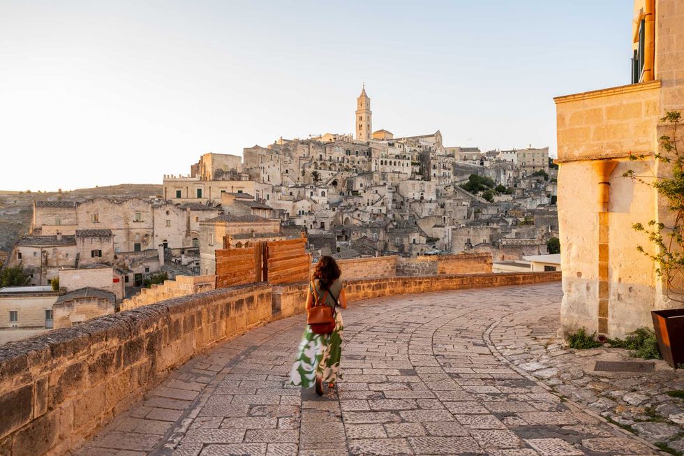 Woman walking on cobblestone path in historic European town at sunset.