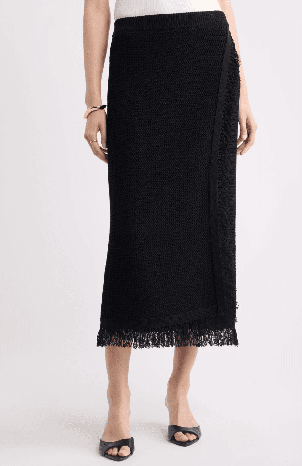 Woman wearing a black fringed midi skirt and black open-toed heels.
