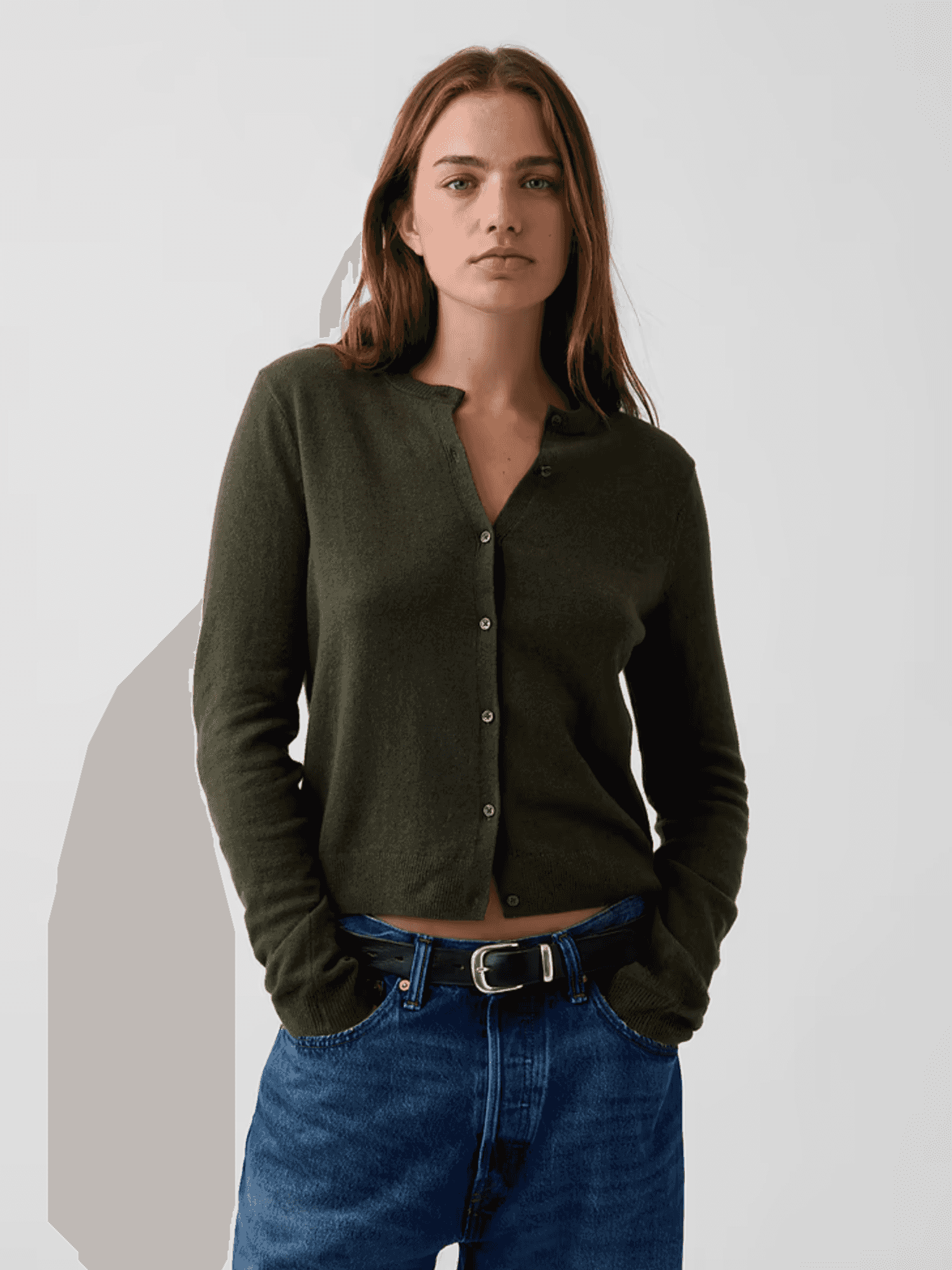 Woman wearing a dark green cardigan and blue jeans, hands in pockets.