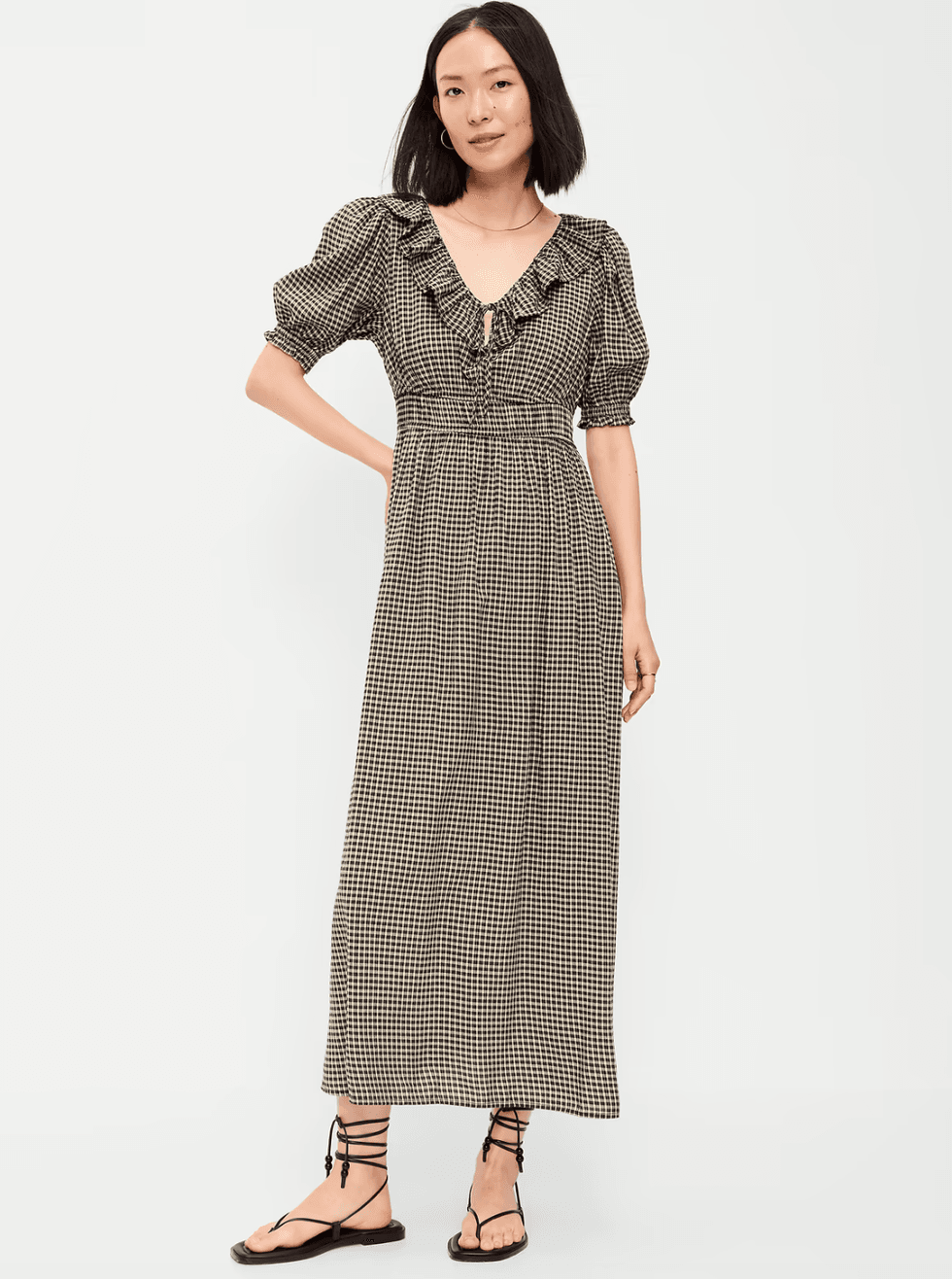 Woman wearing a gingham puff-sleeve dress and black sandals.