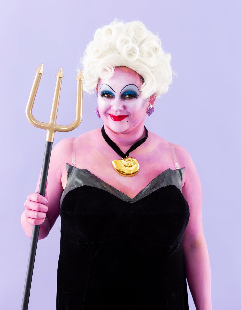 Woman wearing an Ursula Halloween costume in front of a purple background.