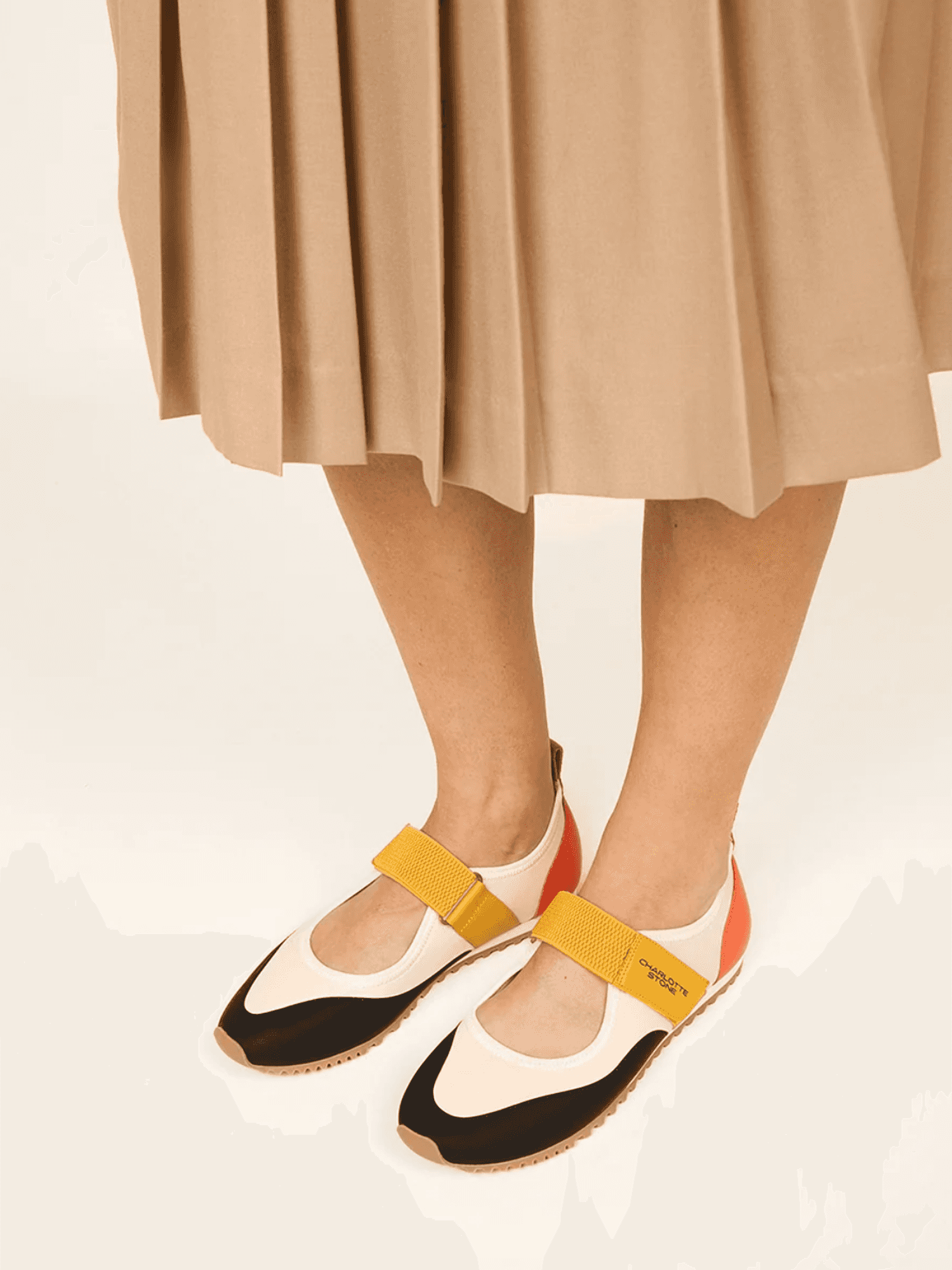 Woman wearing beige skirt and color-block flats with yellow straps.
