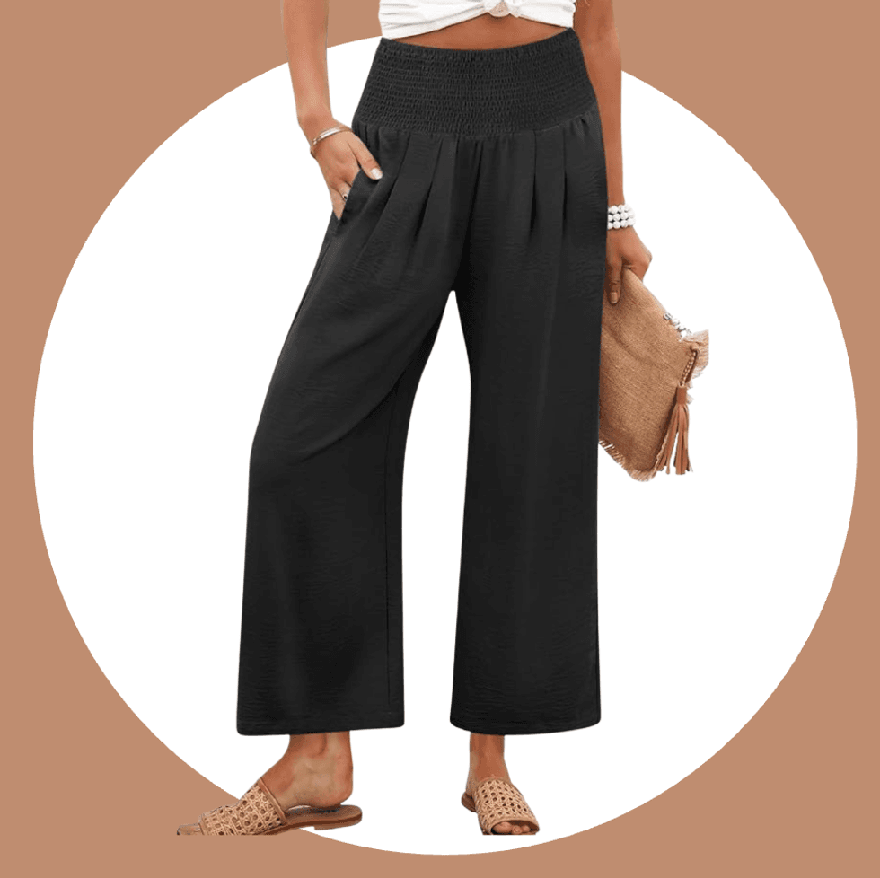 Woman wearing black wide-leg pants, holding a beige clutch and wearing woven sandals.
