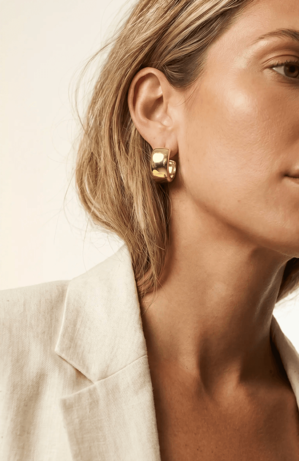 Woman wearing gold hoop earring and beige blazer, side profile.