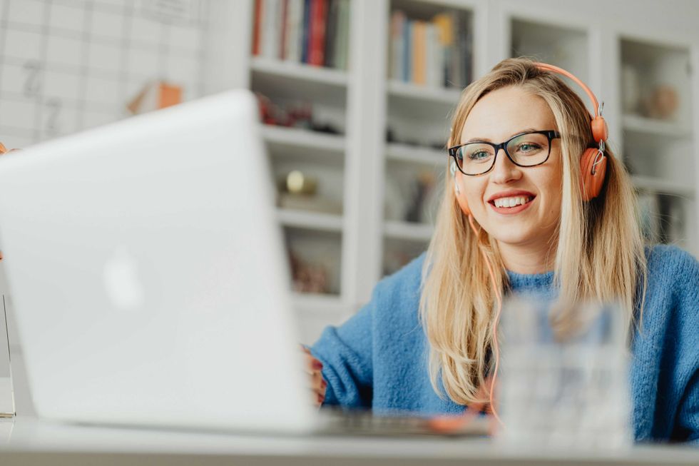 Woman wearing headphones, smiling at a laptop in a bright room.