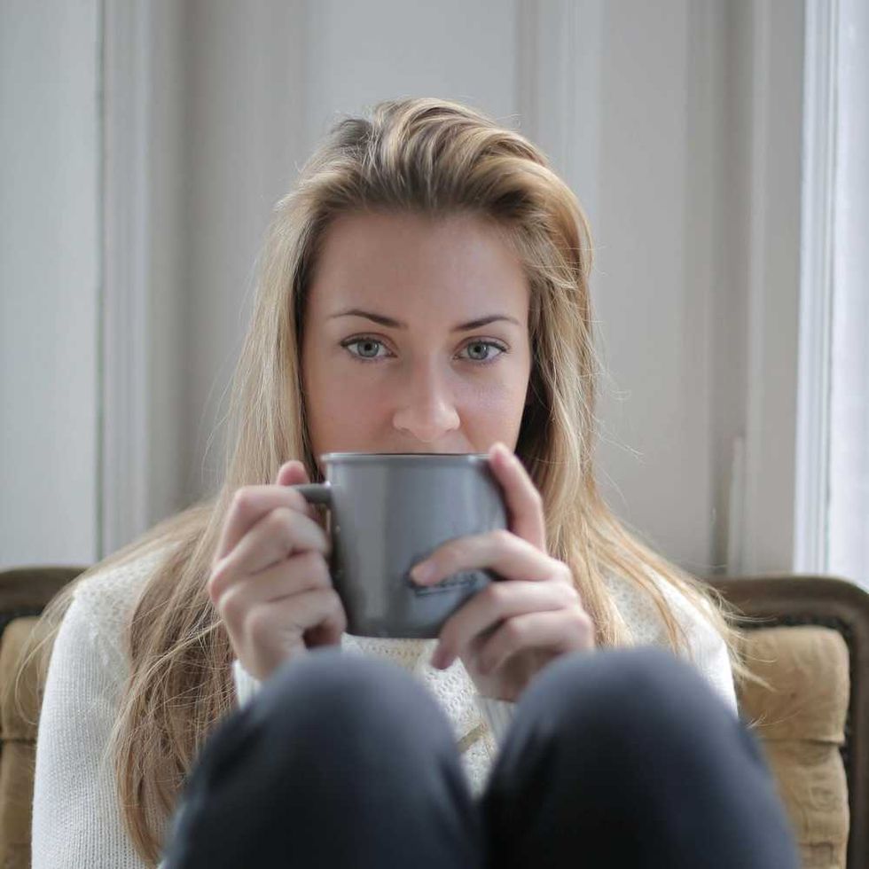 Woman with blonde hair holding a gray mug, seated indoors with light in the background.
