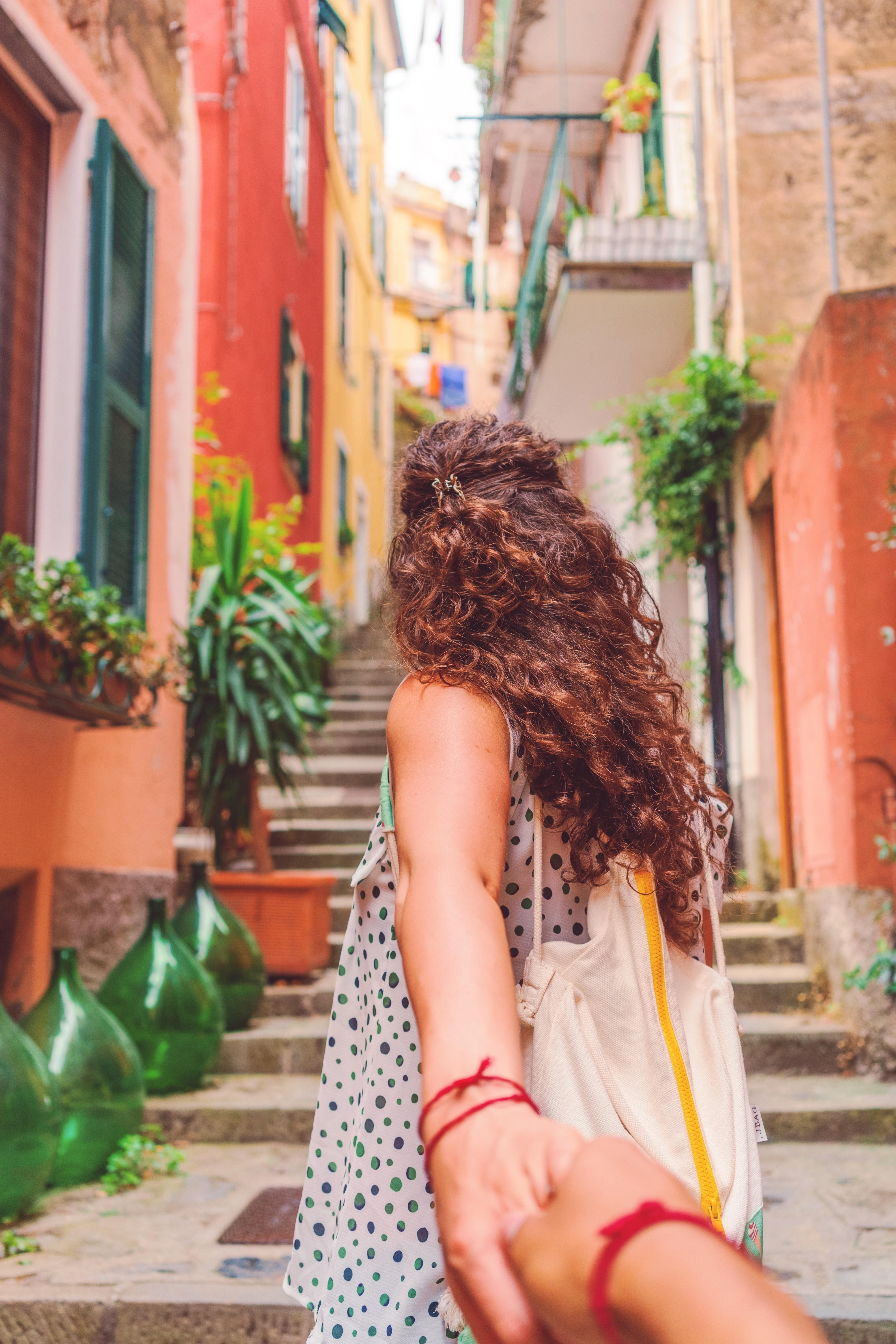 woman with brown hair reaching back to grab hand going up stairs of colorful old homes