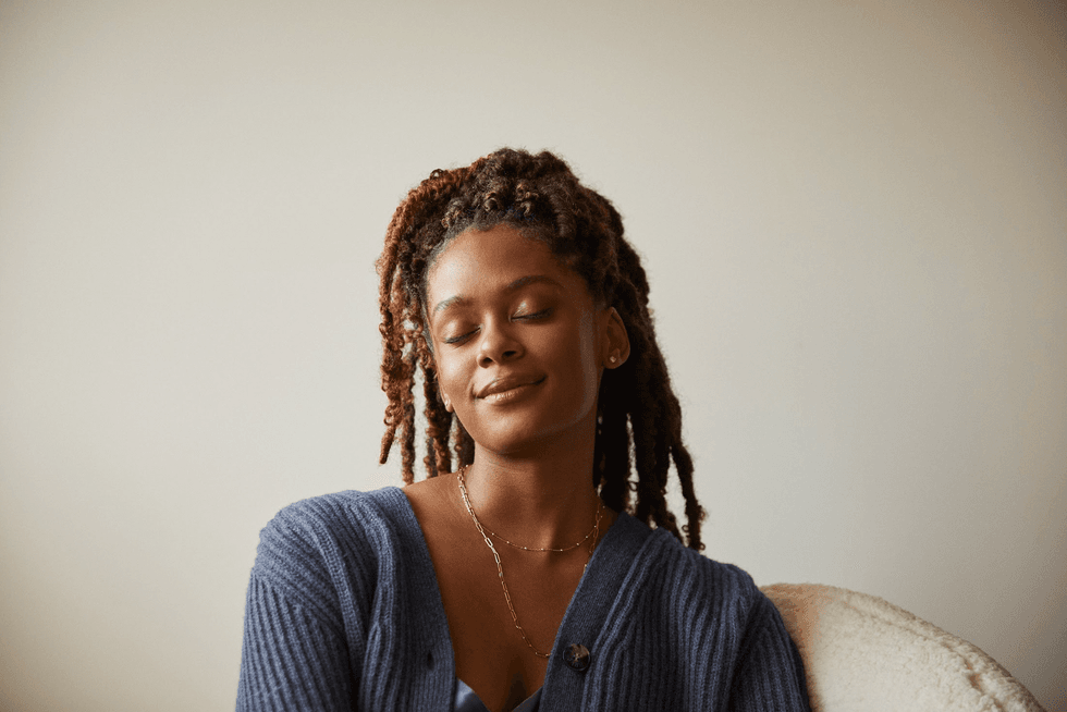 Woman with closed eyes, smiling softly, wearing a blue sweater.