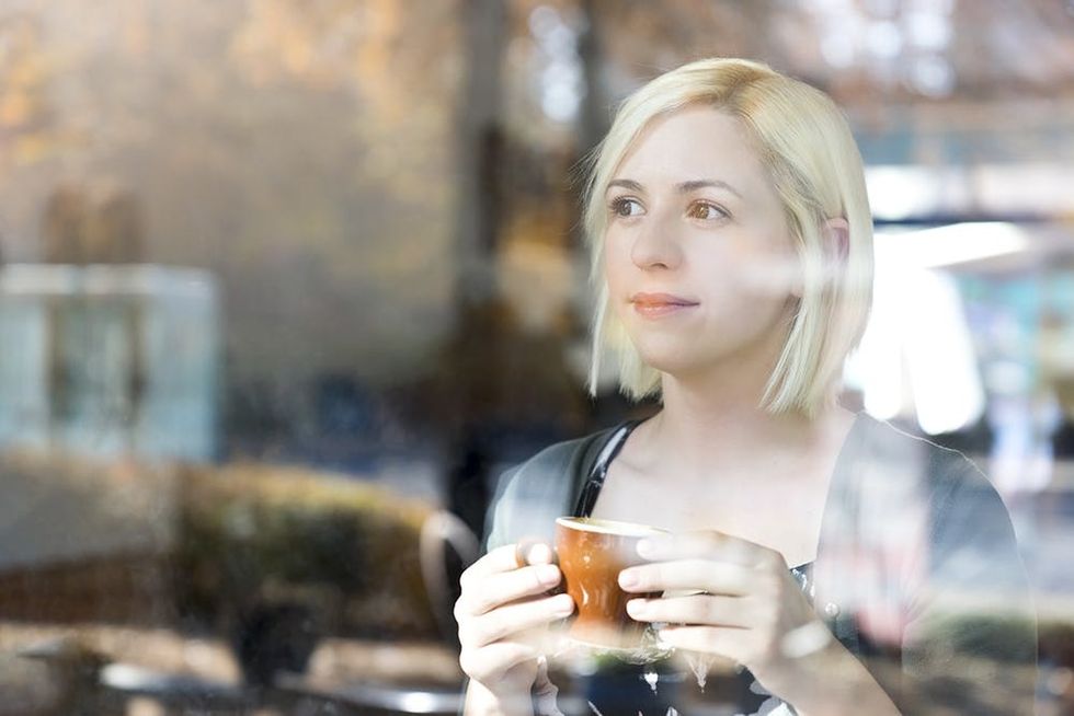 Woman with cup of coffee looking out of window.