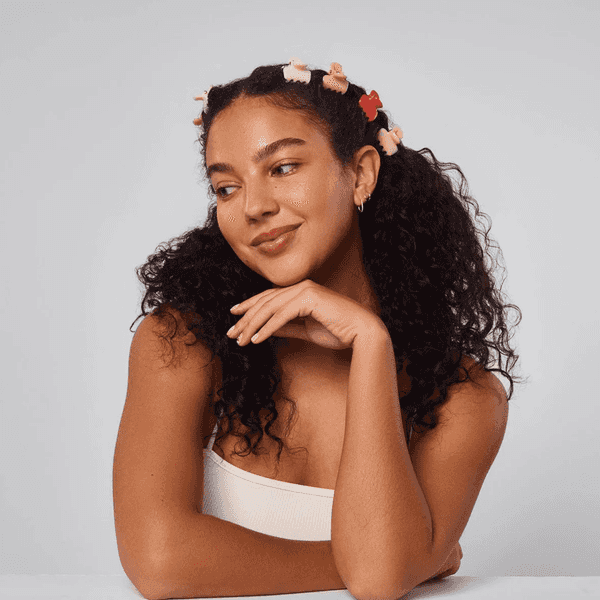 Woman with curly hair and bear clips, resting head on hand, smiling.