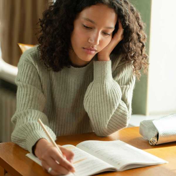Woman with curly hair studying at a table, wearing a gray sweater.