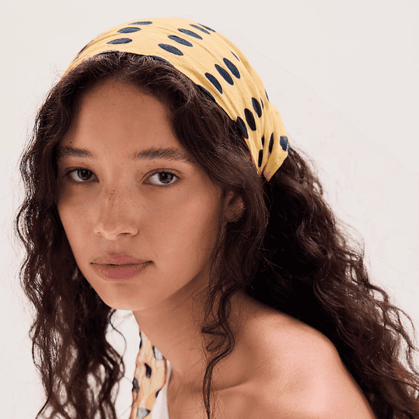 Woman with curly hair wearing a yellow polka dot headscarf.