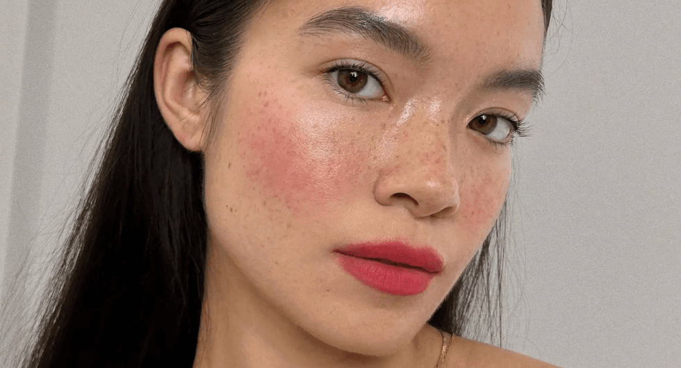 Woman with dewy skin, natural freckles, and pink lips gazes at the camera.