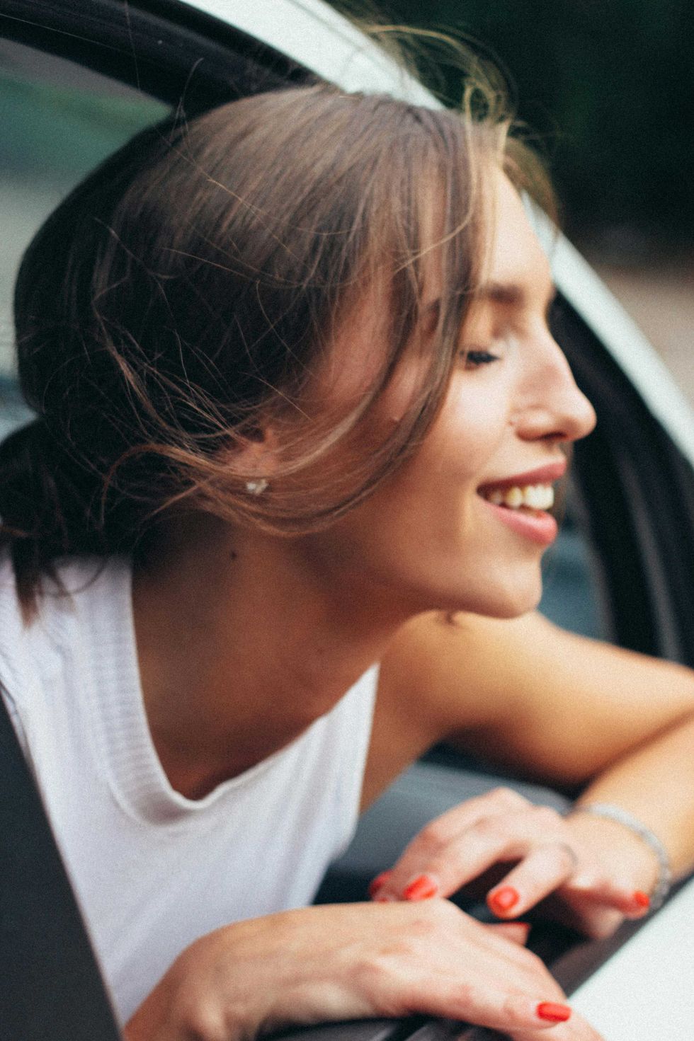 Woman with eyes closed, smiling, leaning out car window.