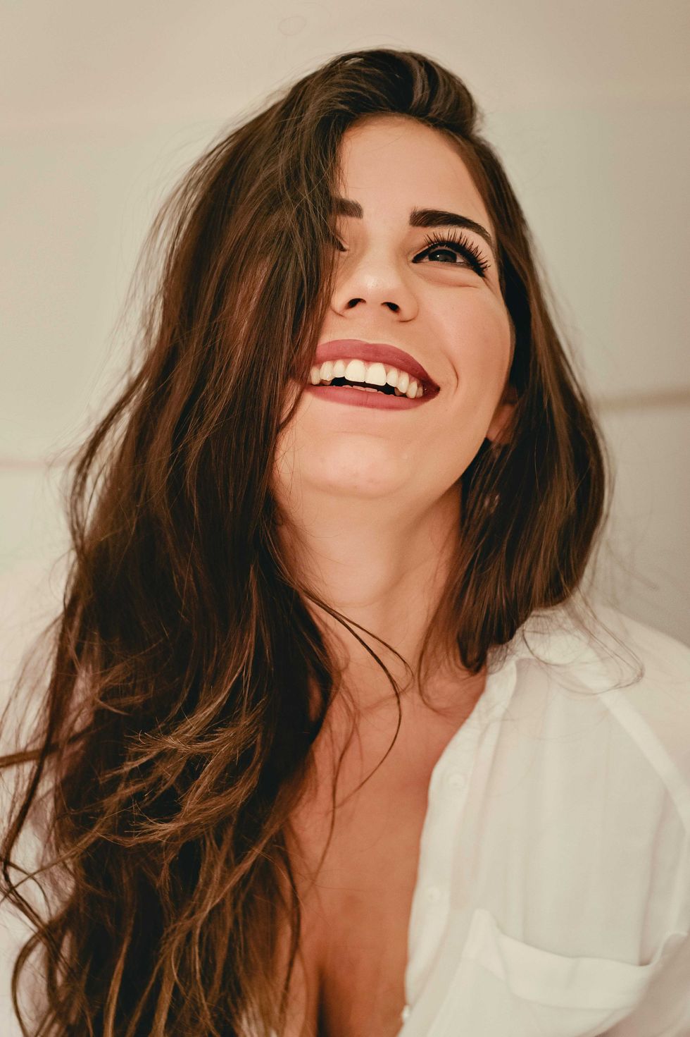 Woman with long brown hair smiling joyfully, wearing a white shirt.
