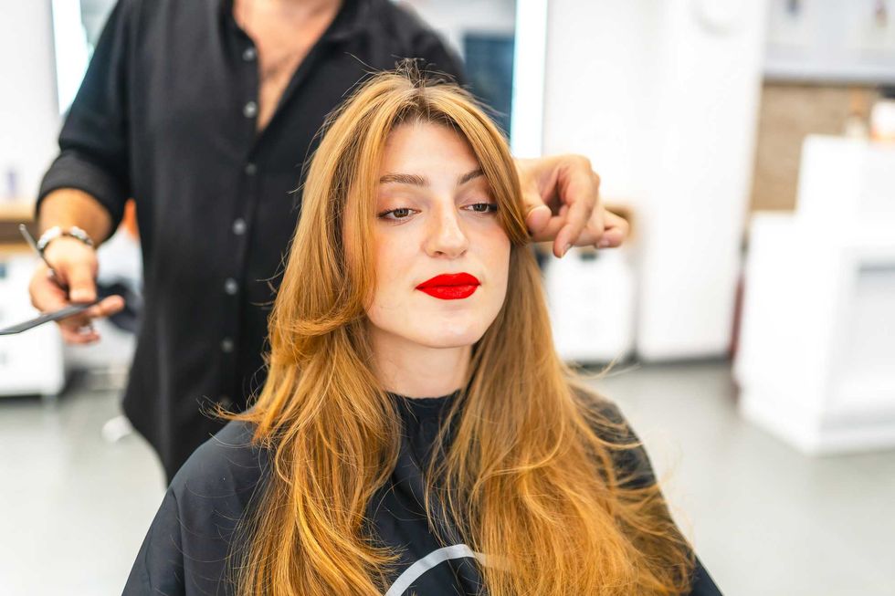 Woman with long hair and red lipstick getting her hair styled in a salon.