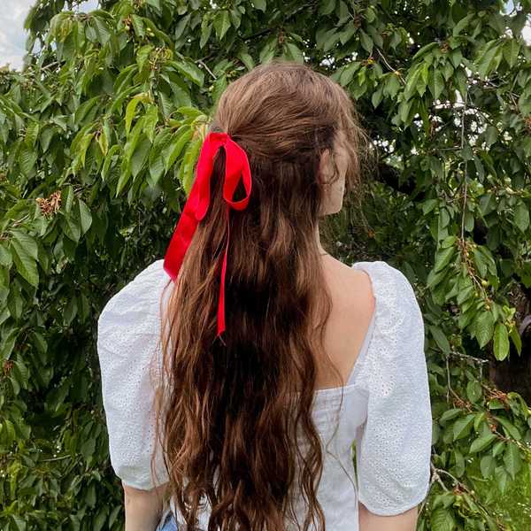 Woman with long hair, red ribbon, white blouse in front of lush green leaves.