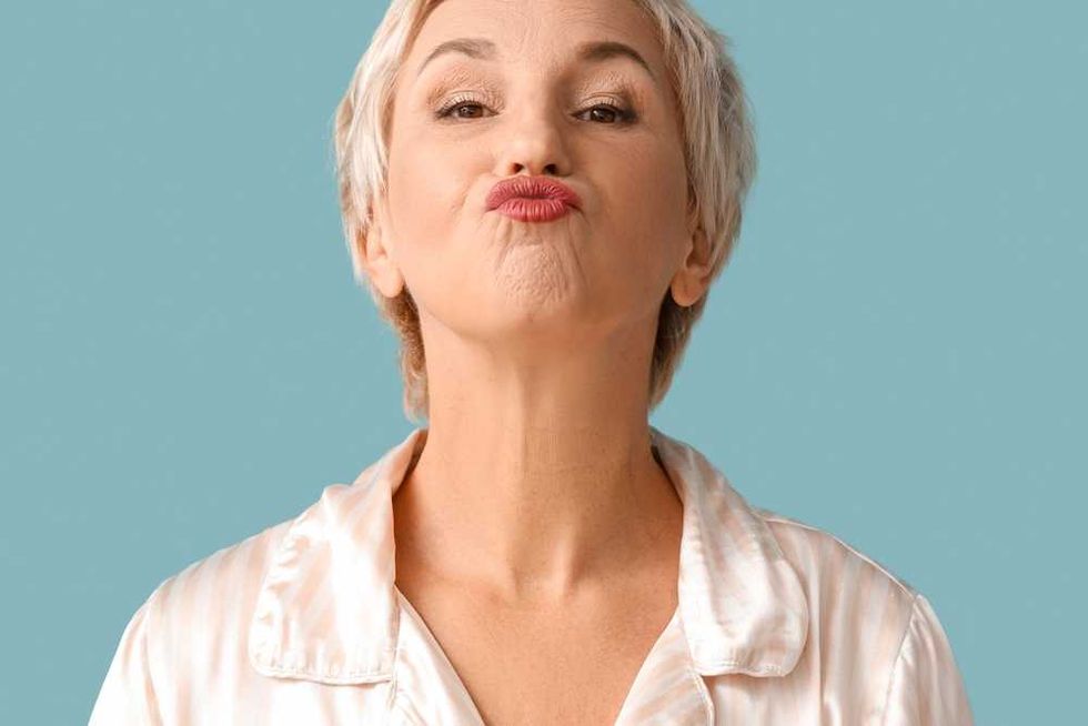 Woman with short hair puckering lips against a blue background.