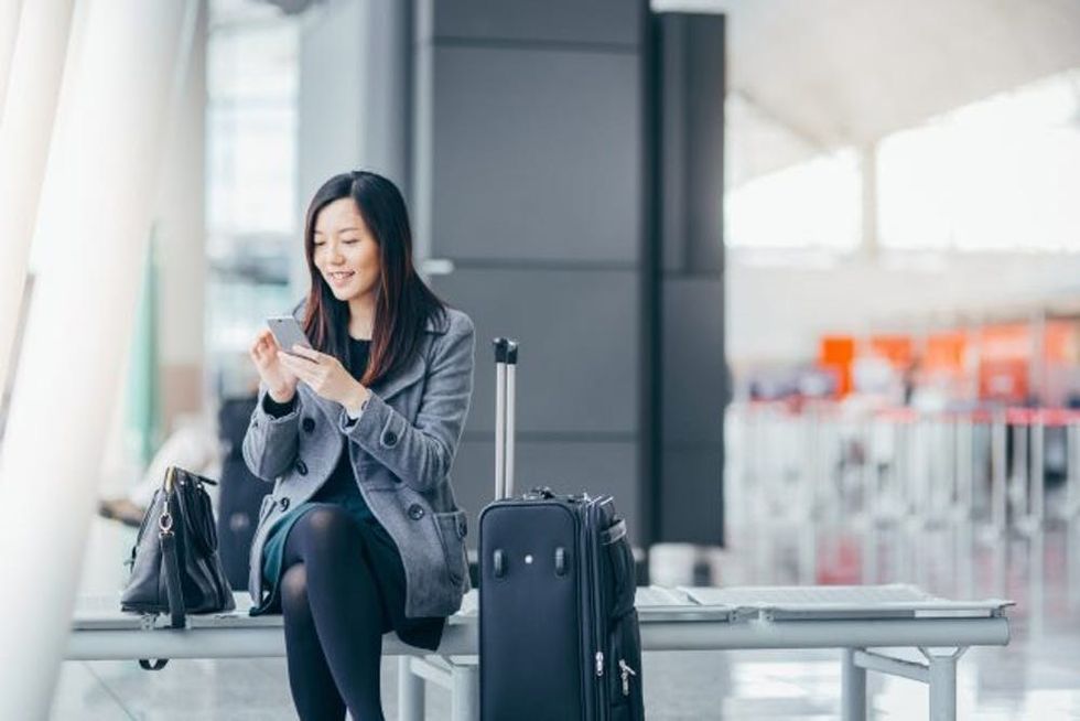 Woman with smartphone and suitcase in airport