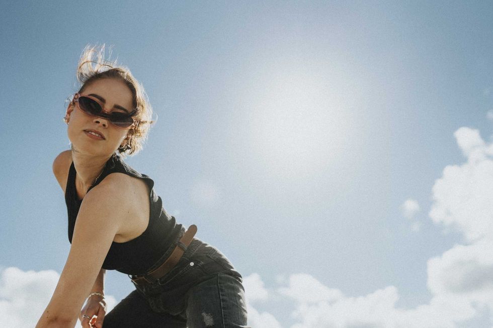 Woman with sunglasses posing against a sunny blue sky.
