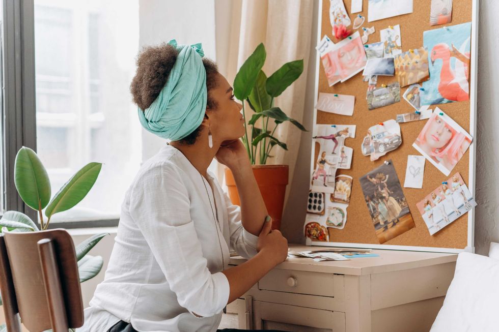 Woman with teal headwrap, pondering at a collage-filled inspiration board.