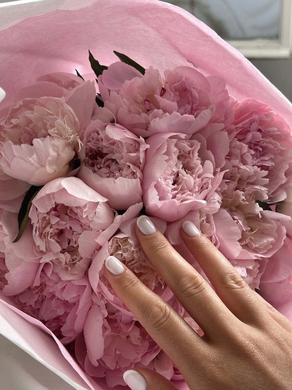 woman with white nails against pink flowers