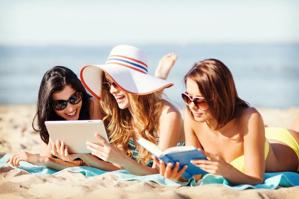 Women share a tablet on a beach