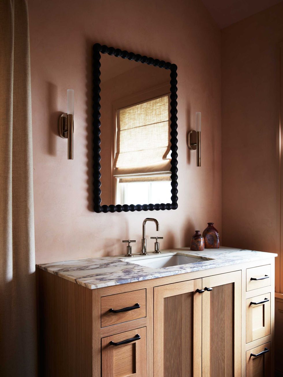Wood vanity with marble top, textured mirror, and sconces in a softly lit bathroom.