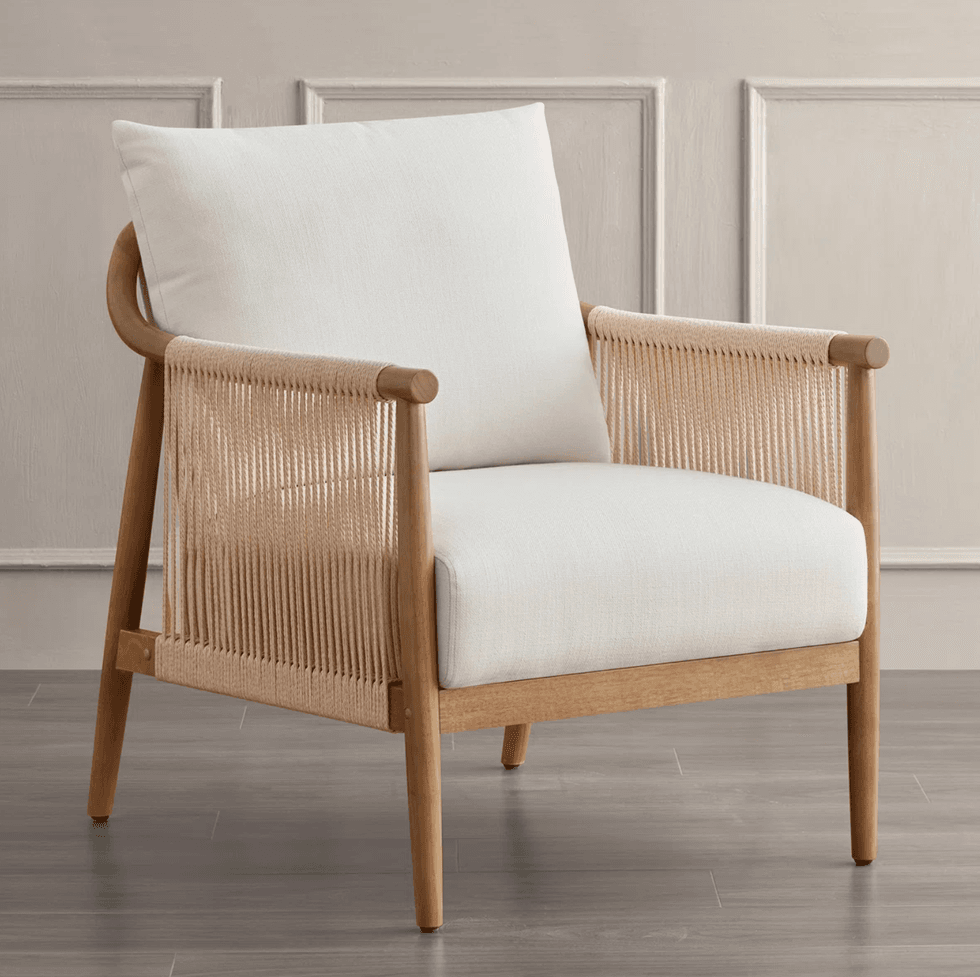 Wooden armchair with white cushions and woven sides on a wooden floor.