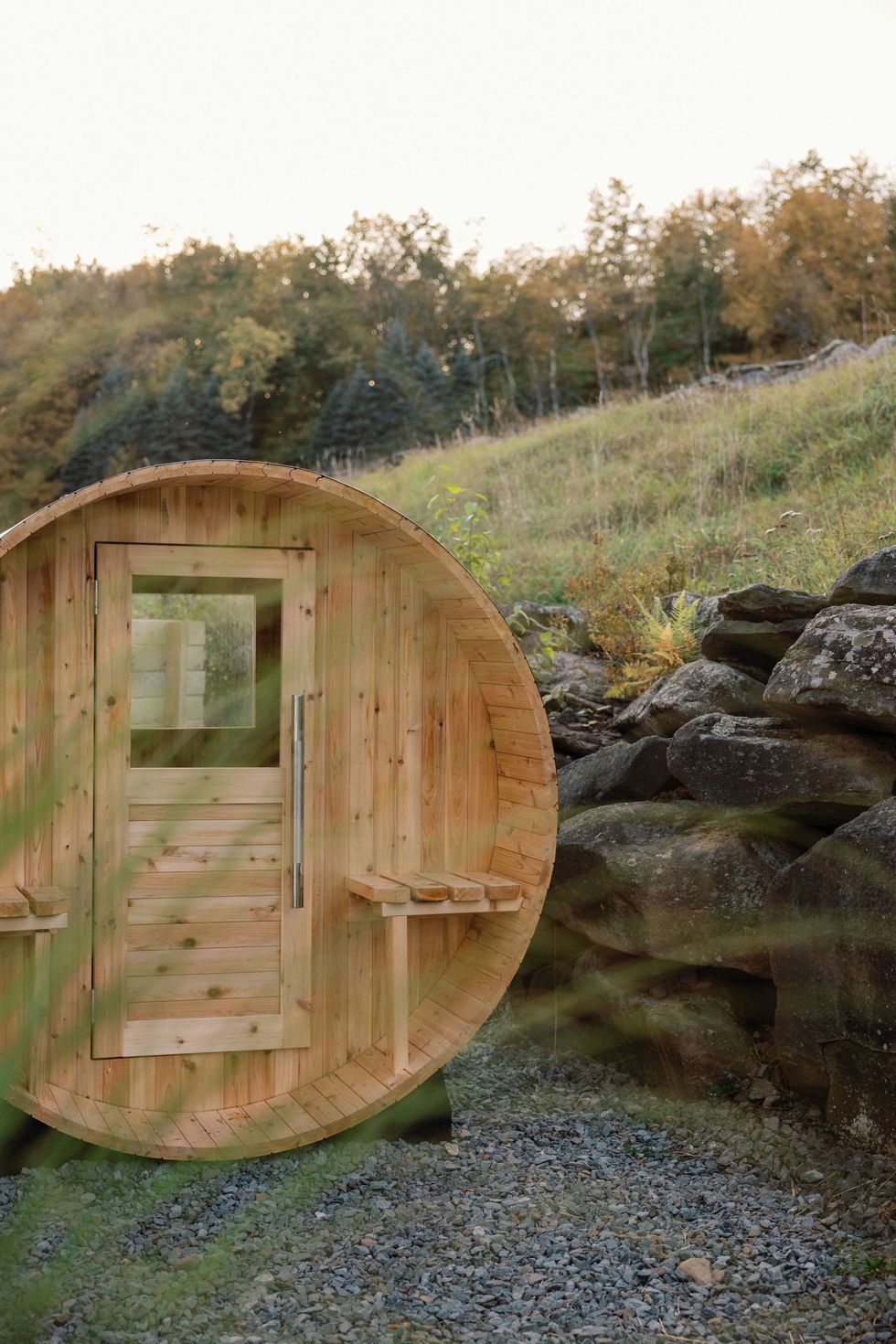 Wooden barrel sauna set in a scenic, grassy hillside landscape.