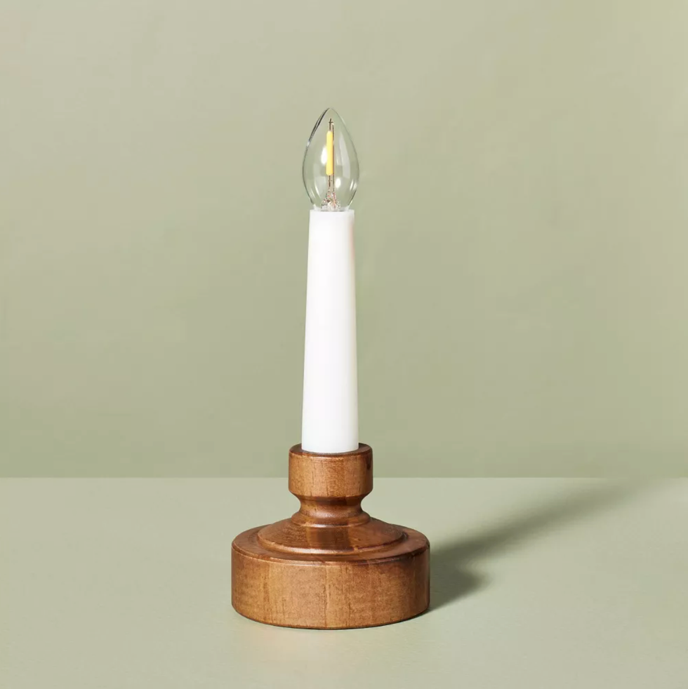 Wooden base candle light with white body and clear bulb on a soft green background.