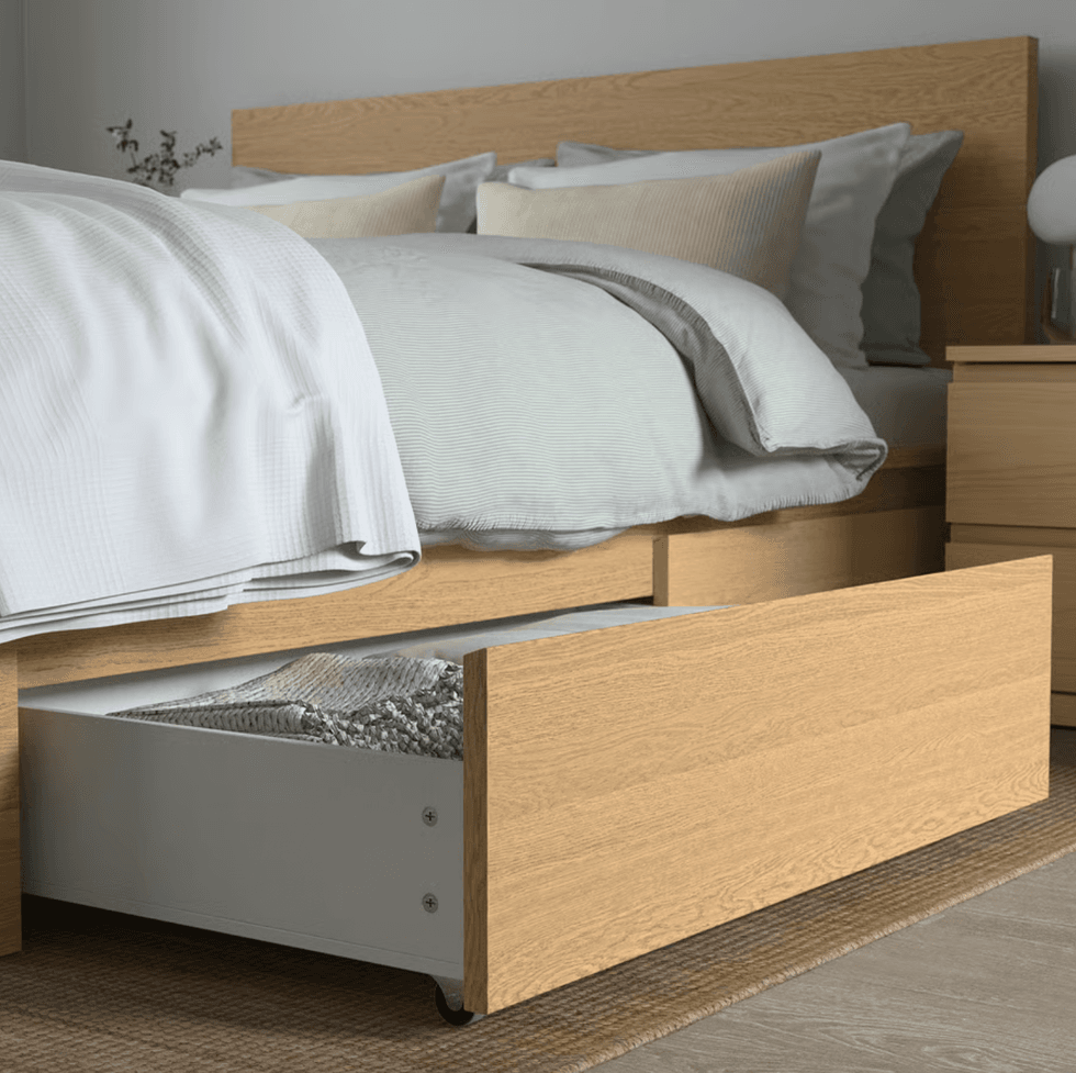 Wooden bed with white linens and an open storage drawer underneath.