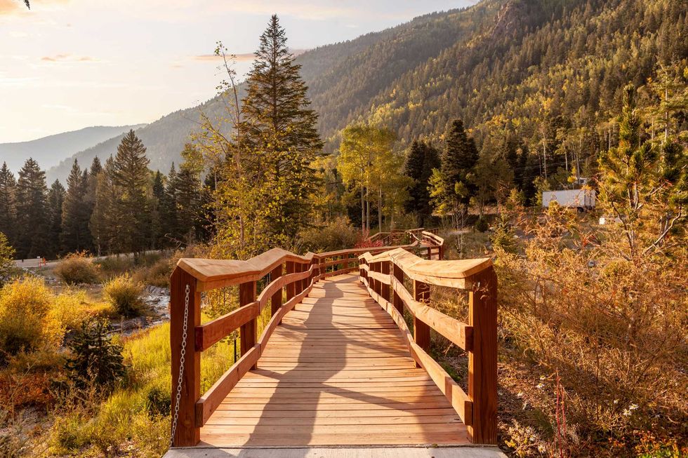 Wooden boardwalk through a forested mountain landscape in warm sunlight.