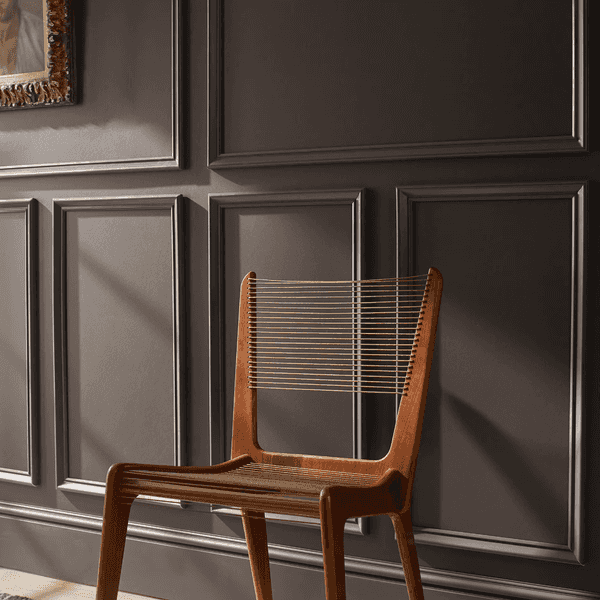 Wooden chair with slatted back against a paneled dark wall, near artwork.