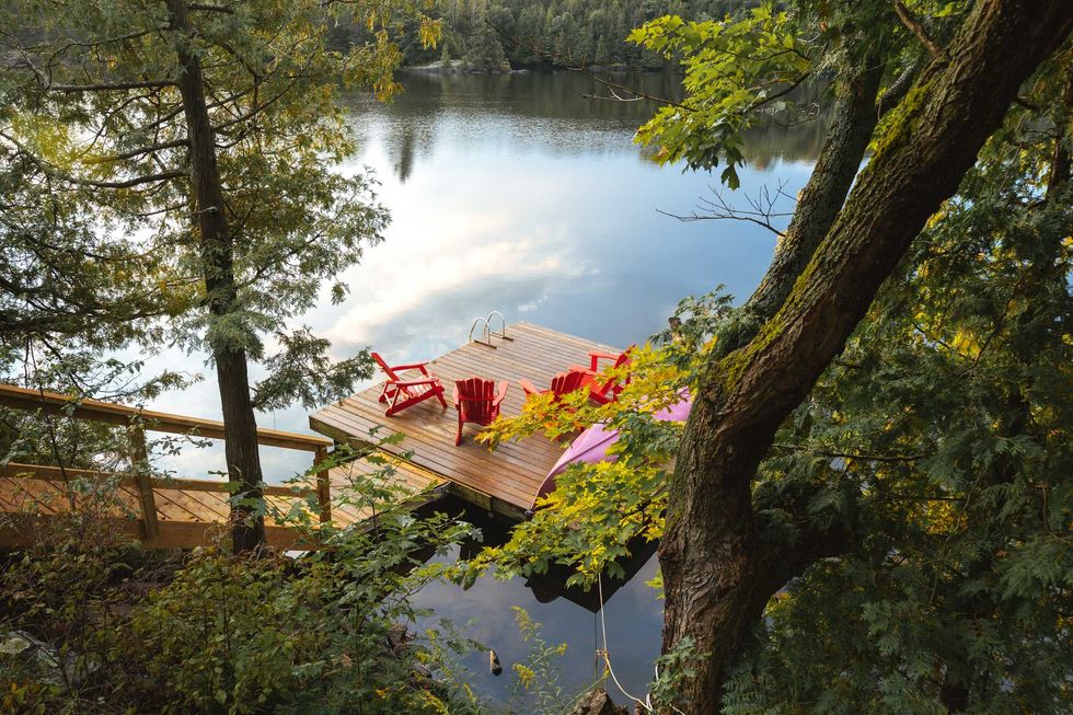 Wooden deck on a tranquil lake with red chairs, surrounded by trees.