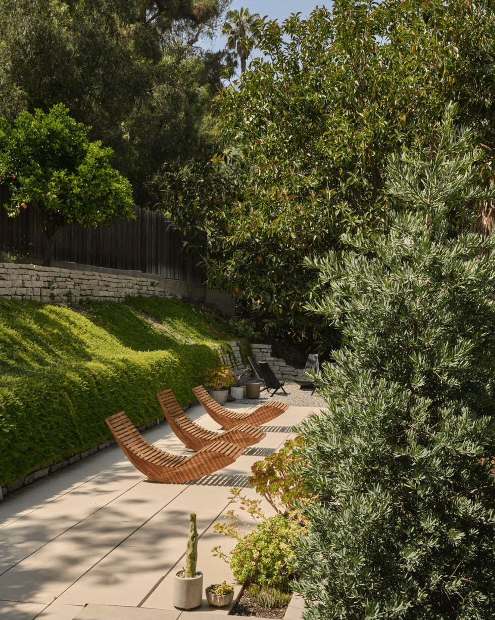 Wooden loungers on a sunlit patio surrounded by lush greenery.