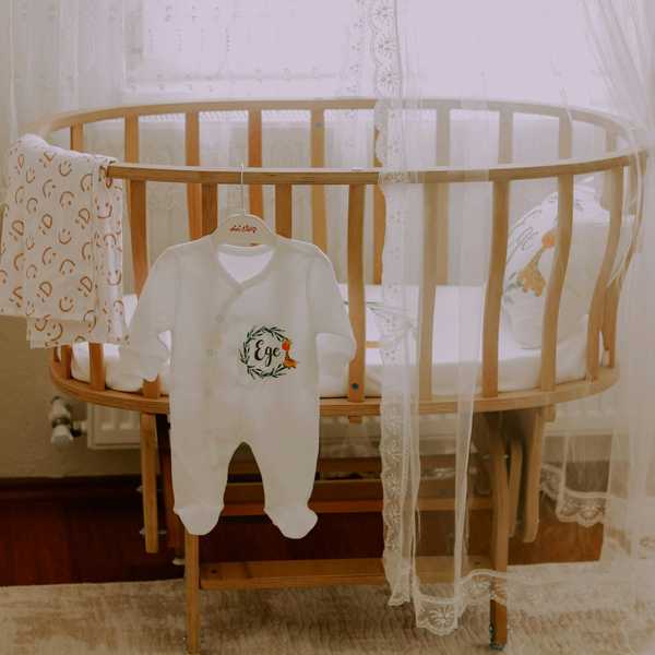 Wooden round crib with lace, onesie, and blanket hanging.
