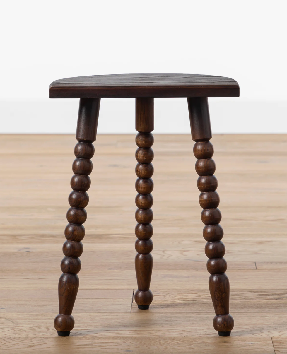 Wooden stool with rounded legs and a simple seat on wooden floor.