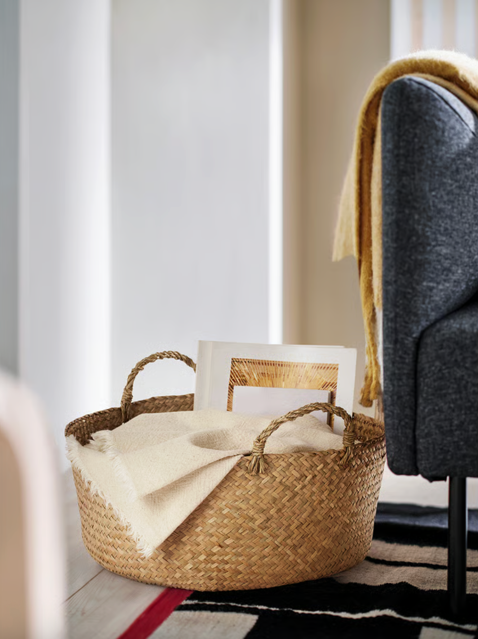 Woven basket with a blanket and framed picture beside a sofa.