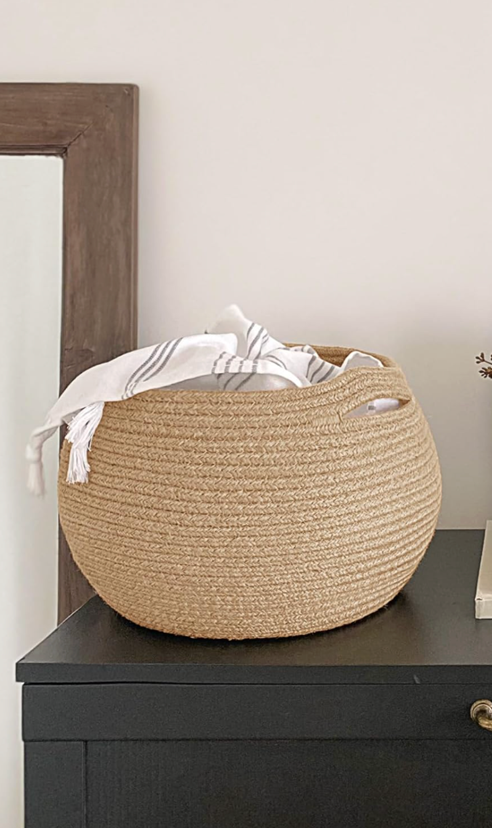 Woven basket with striped towel on black surface near mirror and beige wall.