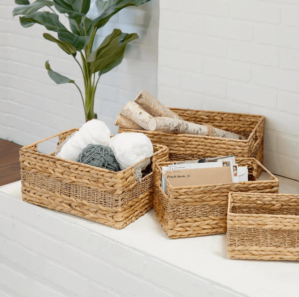 Woven baskets with yarn, logs, and mail on a white shelf beside a green plant.