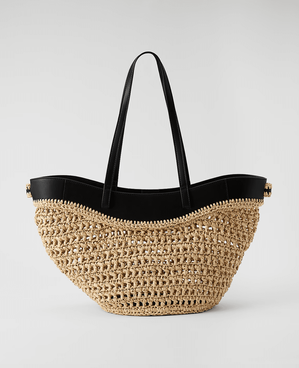 Woven straw bag with black leather straps and trim, on a plain background.