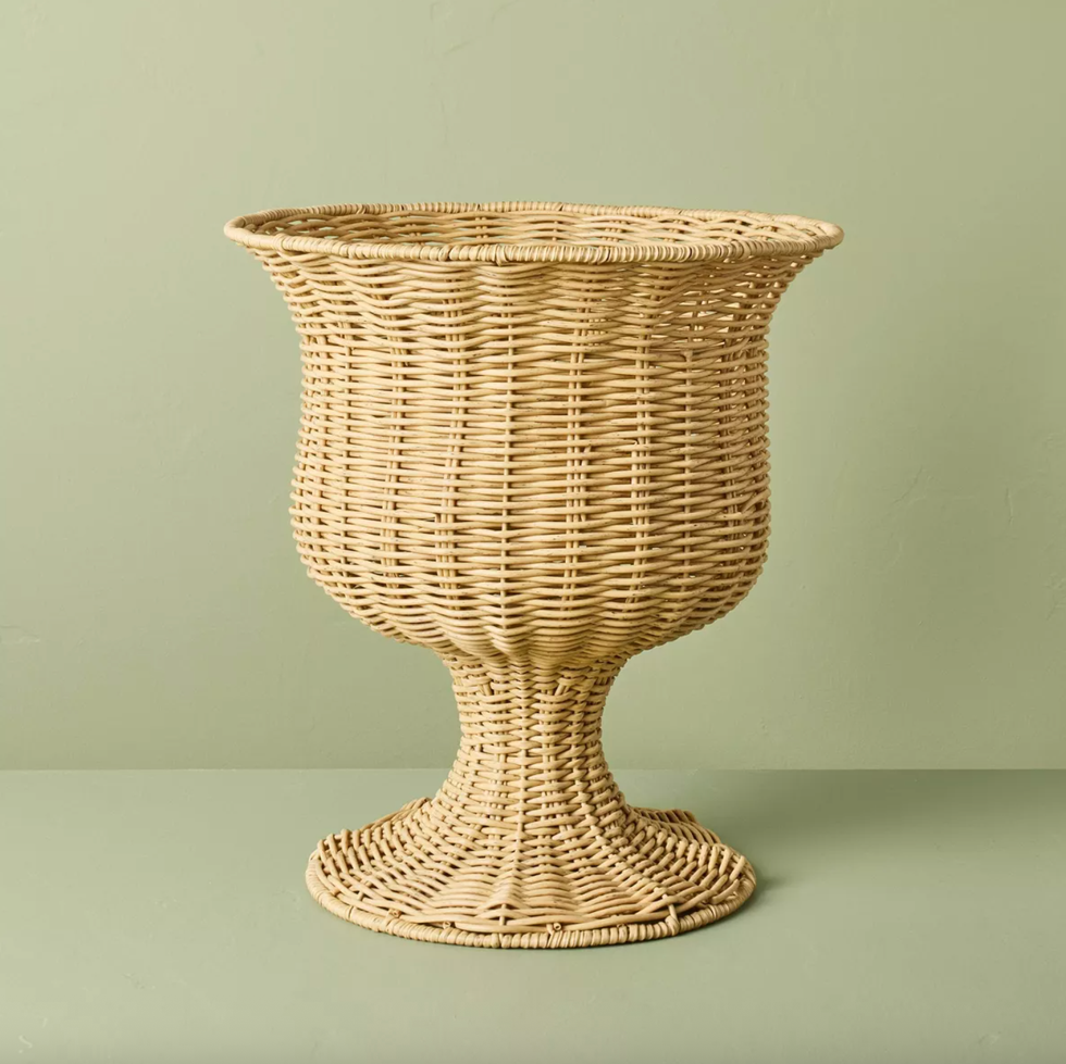 Woven wicker pedestal basket on a light green background.