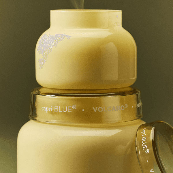 Yellow candle jar with capri BLUE logo and "VOLCANO" text, emitting light smoke.
