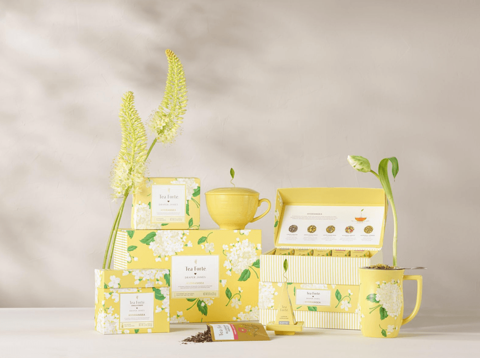 Yellow tea set with floral design, boxes, and flowers, arranged on a white surface.