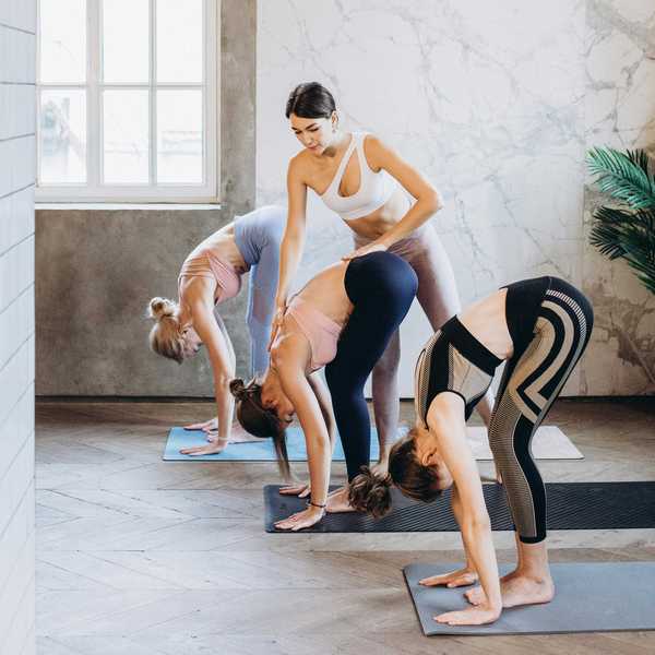 Yoga instructor guides three women in forward bend pose in a studio.