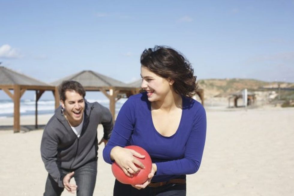 Young couple running with ball on beach, Tel Aviv, Israel