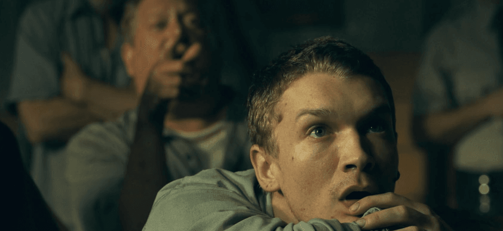 Young man in suspenseful viewing; older man in background pointing, others blurred.